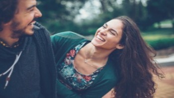 A young couple stands outside, laughing hard with each other. 