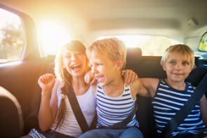 Three young children laughing in the backseat of a car. 